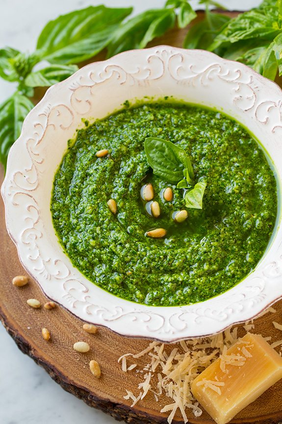 Basil Pesto in white bowl next to wedge of Parmesan and fresh basil leaves