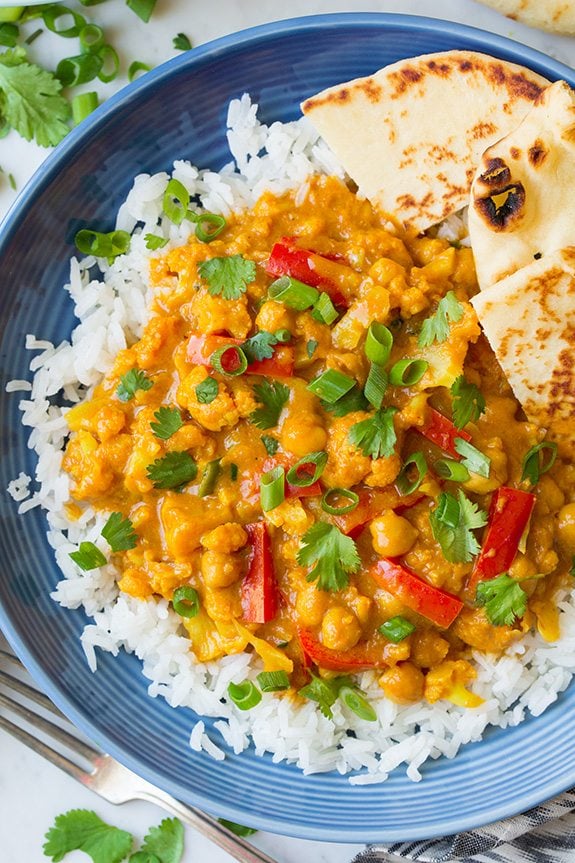 Red Vegetable Curry Vegetable curry over rice in a blue bowl. Ingredients include cauliflower, red bell pepper, onion, cilantro and a curry sauce.