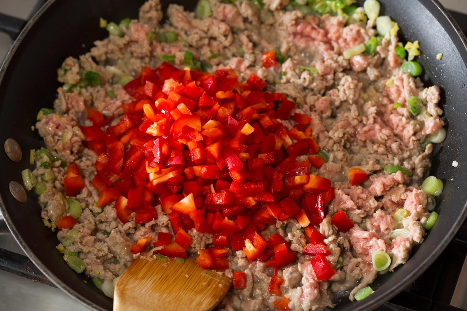Thai Chicken Lettuce Wraps Chopped bell peppers being added to the ground meat in the skillet.
