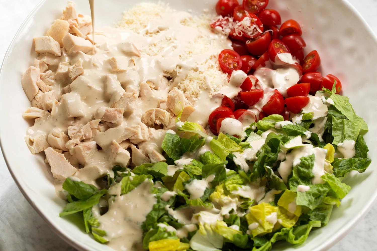 Chicken Caesar Wrap Dressing added to chicken caesar salad ingredients in mixing bowl.