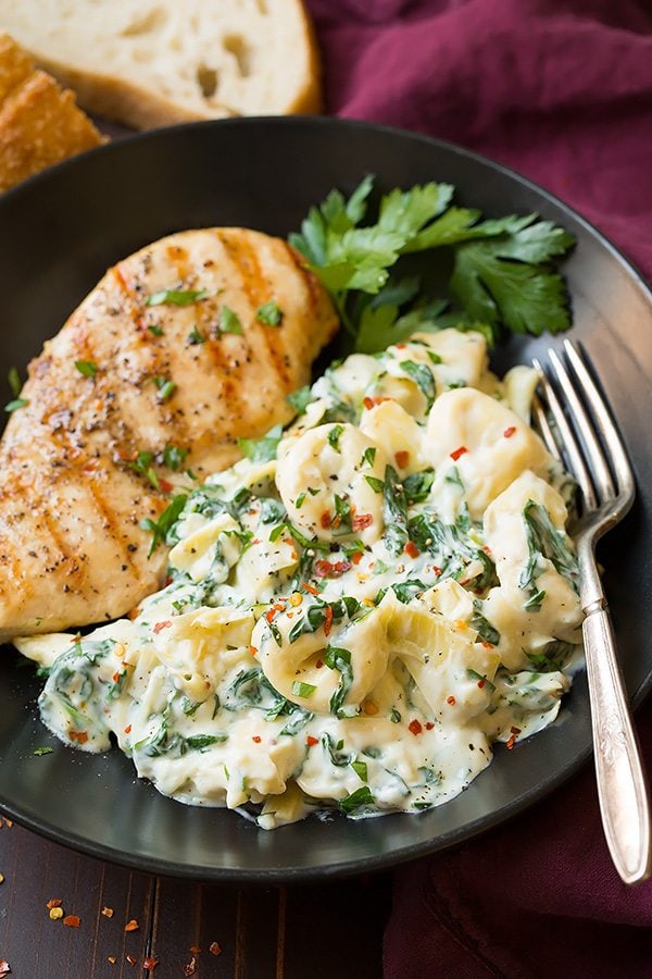 Creamy Spinach Artichoke Tortellini served in a black matte plate with chicken breasts.