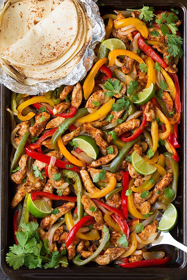 Sheet Pan Chicken Fajitas Chicken fajita mixture on a sheet pan with a side of tortillas. Fajita mixture includes seasoned chicken strips, bell peppers, onions and cilantro.