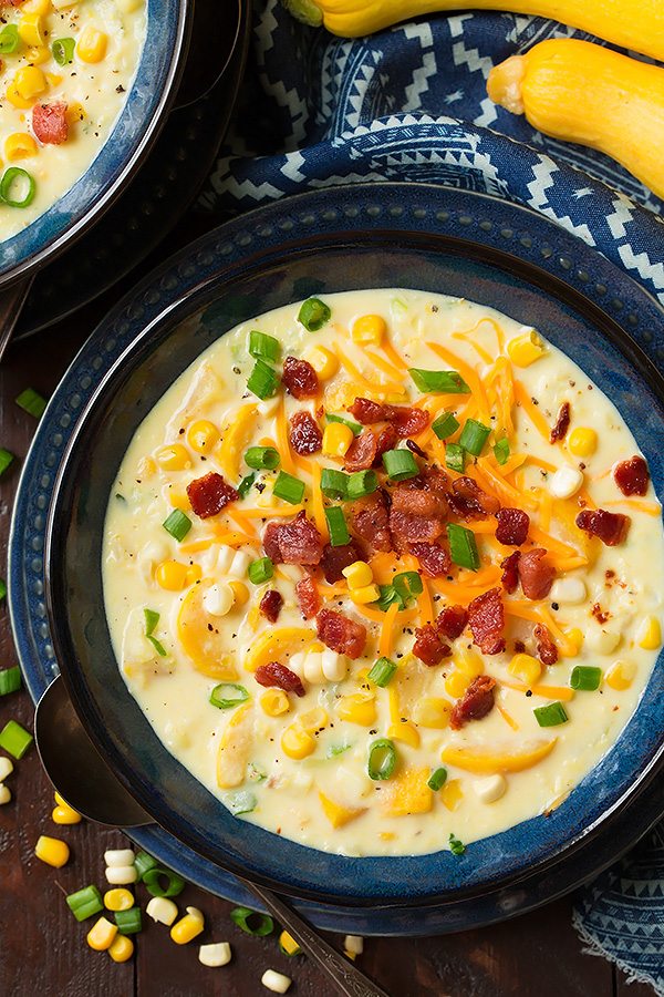 Summer Squash and Corn Chowder Summer Squash and Corn Chowder in a blue serving bowl set over a blue plate. It's garnished with shredded cheddar, bacon and green onions.