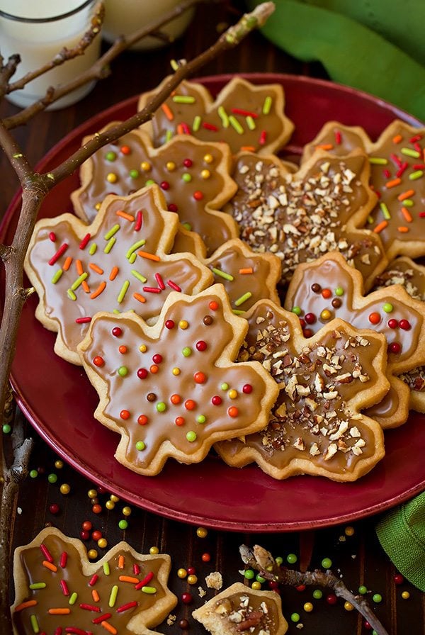 Glazed Maple Shortbread Cookies Glazed Maple Shortbread Cookies cut into leaf shapes and sitting on a maroon plate. There's a branch for decoration to the side and a green napkin.