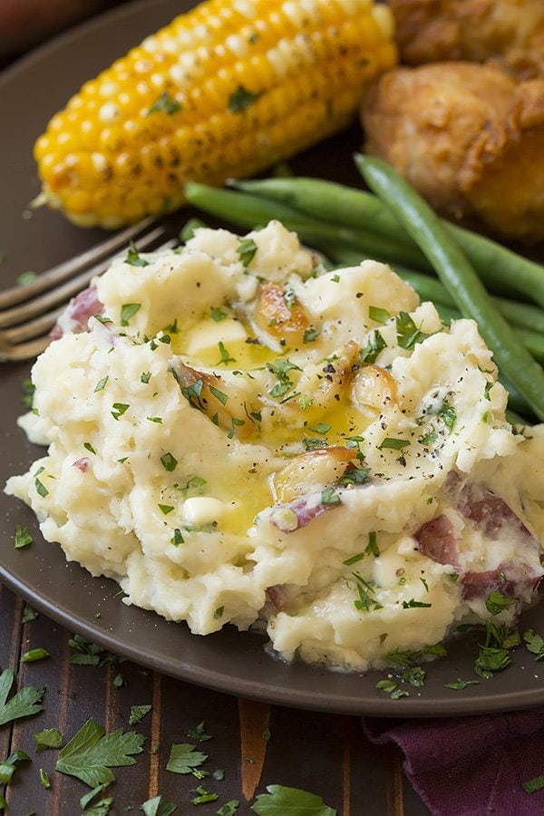 Roasted Garlic Mashed Potatoes Serving of garlic mashed potatoes on a matte brown serving plate with a side of green beans, chicken and corn.