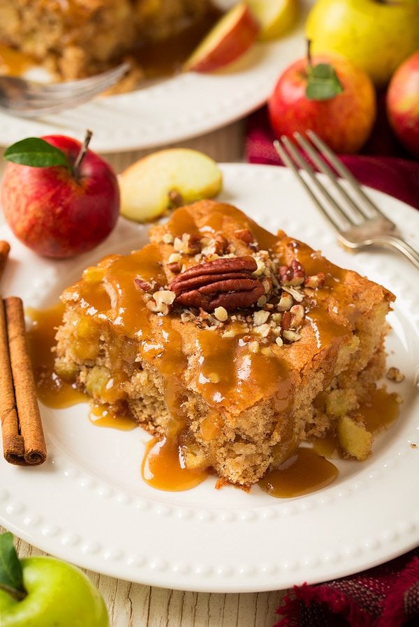 Warm Apple Cake Apple cake with a caramel sauce served on a white plate that's decorated with apples and cinnamon sticks.