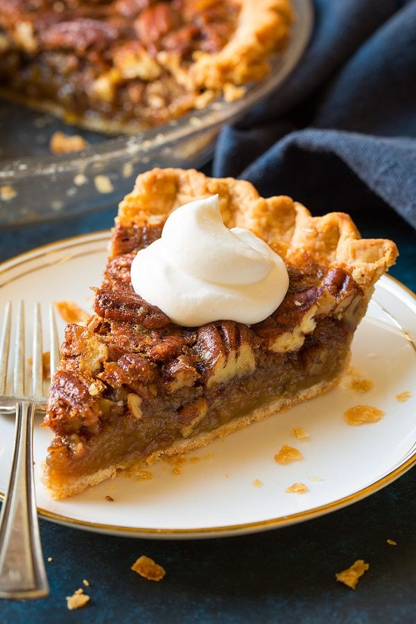 Pecan Pie Recipe Slice of pecan pie on a white dessert plate. Pie is topped with whipped cream.