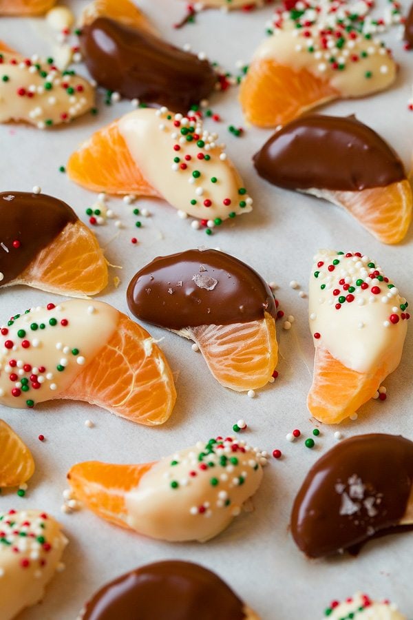 Chocolate Dipped Oranges Chocolate dipped mandarin oranges on parchment paper, some are covered with Christmas sprinkles or sea salt.