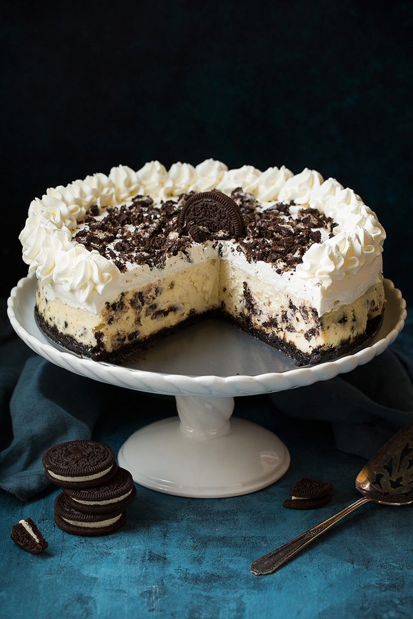 Oreo Cheesecake Oreo cheesecake on a cake stand with about 1/3 of the cake cut from one section to show inside of cheesecake.