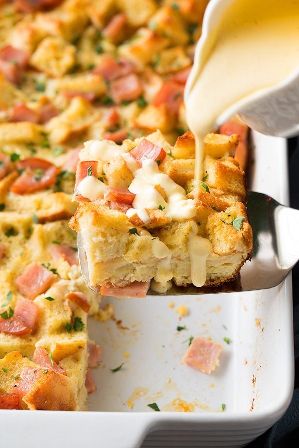 Eggs Benedict Casserole Pouring hollandaise sauce over eggs benedict casserole.