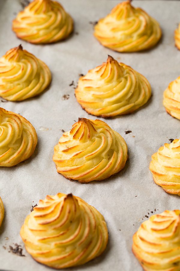 Garlic Parmesan Duchess Potatoes Duchess potatoes on a parchment paper lined baking sheet after baking.