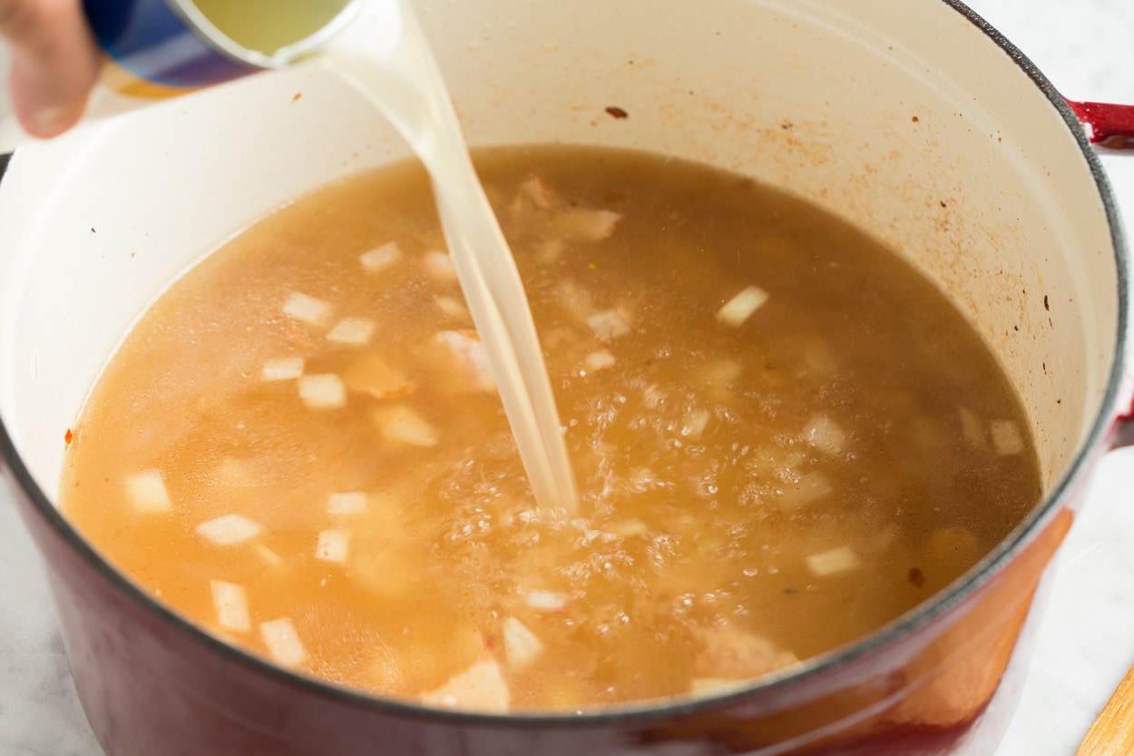 Pour chicken broth into mixture in pot for zuppa toscana.