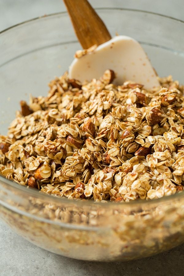 Granola Recipe Mixing granola in a glass bowl. Mixture includes, oats, flax seeds, almonds, honey, brown sugar, almond and vanilla extract, coconut oil.