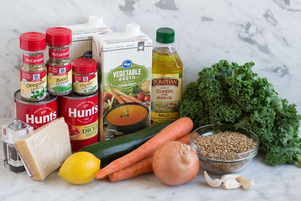 Lentil Soup Ingredients needed to make lentil soup show n here including dry lentils, kale, onion, garlic, zucchini, lemon, vegetable broth, olive oil, canned tomatoes, dried herbs and parmesan.