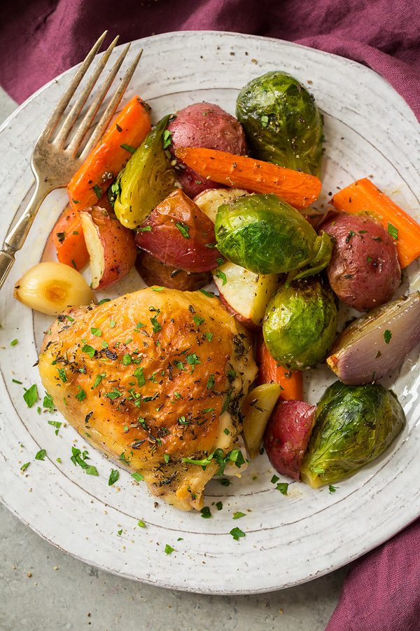 Sheet Pan Chicken and Veggies Roasted chicken thigh and roasted vegetables on a white serving plate.