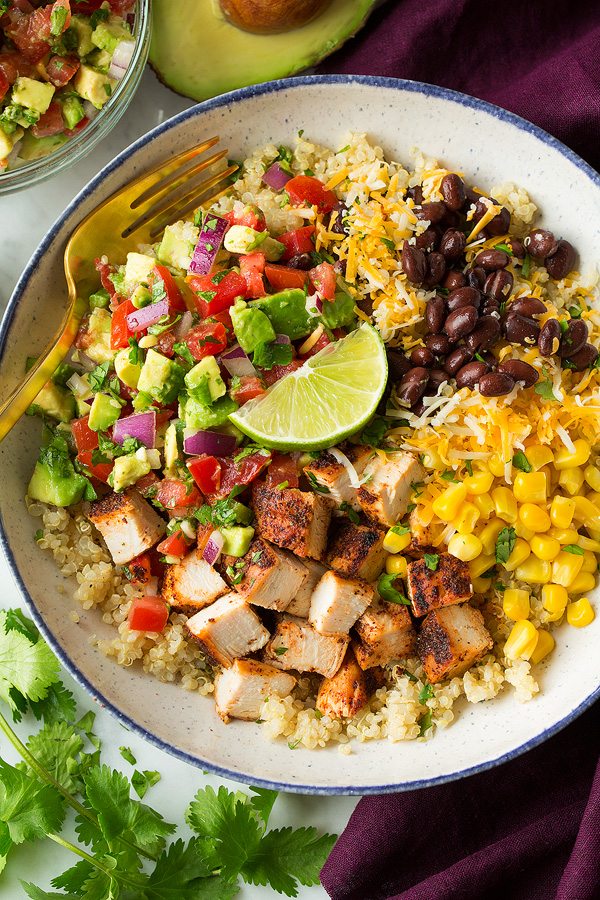 Grilled Chicken Burrito and Quinoa Bowls with Avocado Salsa chicken Burrito bowls layered with quinoa, grilled chicken, black beans, corn, cheese and avocado salsa. Shown here in a white speckled bowl sitting on a marble surface.
