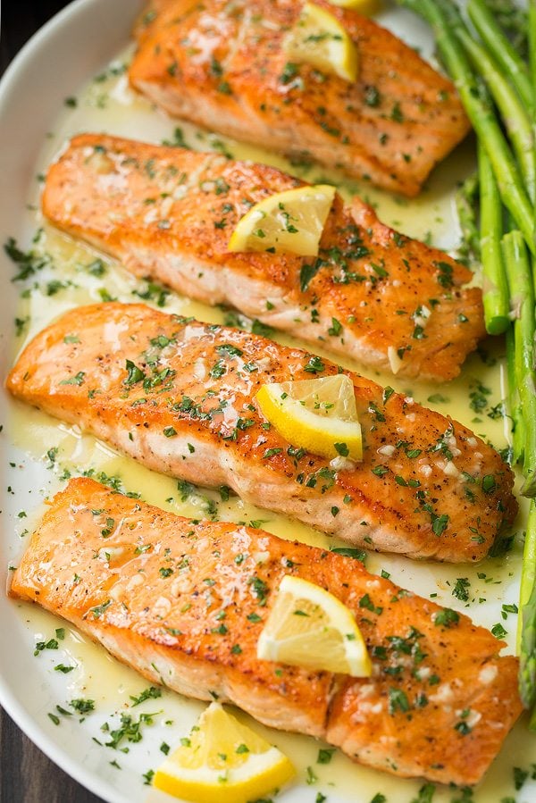 pan seared salmon fillets on a serving platter topped with a garlic lemon butter sauce. Served with a side of asparagus.