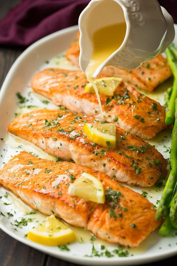 Skillet Seared Salmon with Garlic Lemon Butter Sauce. A delicious and easy meal that's perfect for weeknights. | Salmon Recipes | Fish Recipes | Weeknight Meals | #salmon #fish #cookingclassy Pouring lemon butter sauce over pan fried salmon fillets on a white platter.