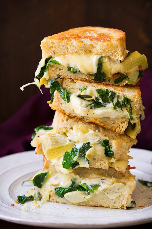 Stack of four grilled cheese sandwich halves on a white plate. Filling includes cheese, spinach and artichokes.