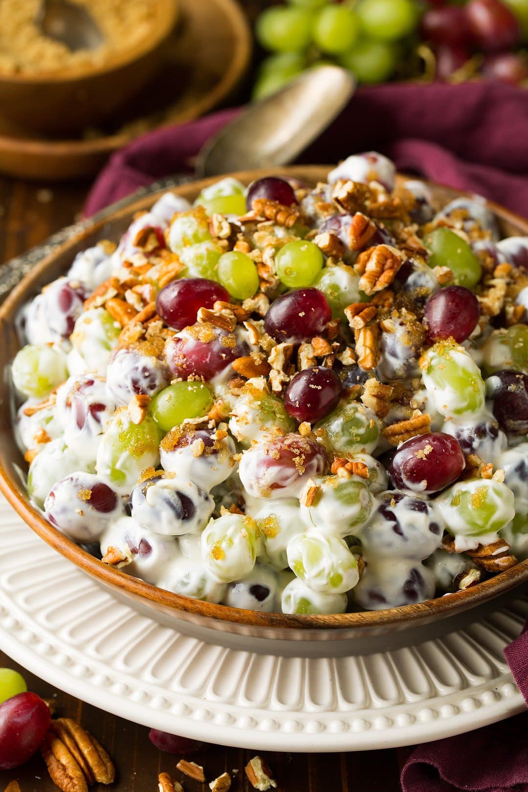 Grape Salad Grape salad toss with a cream cheese dressing and pecans. Served in a wooden bowl over a white scalloped plate.
