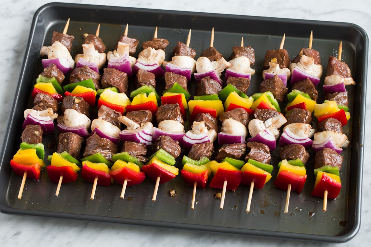 Best Steak Kebabs Kebabs ingredients threaded onto skewers, shown before grilling aligned on a baking sheet.