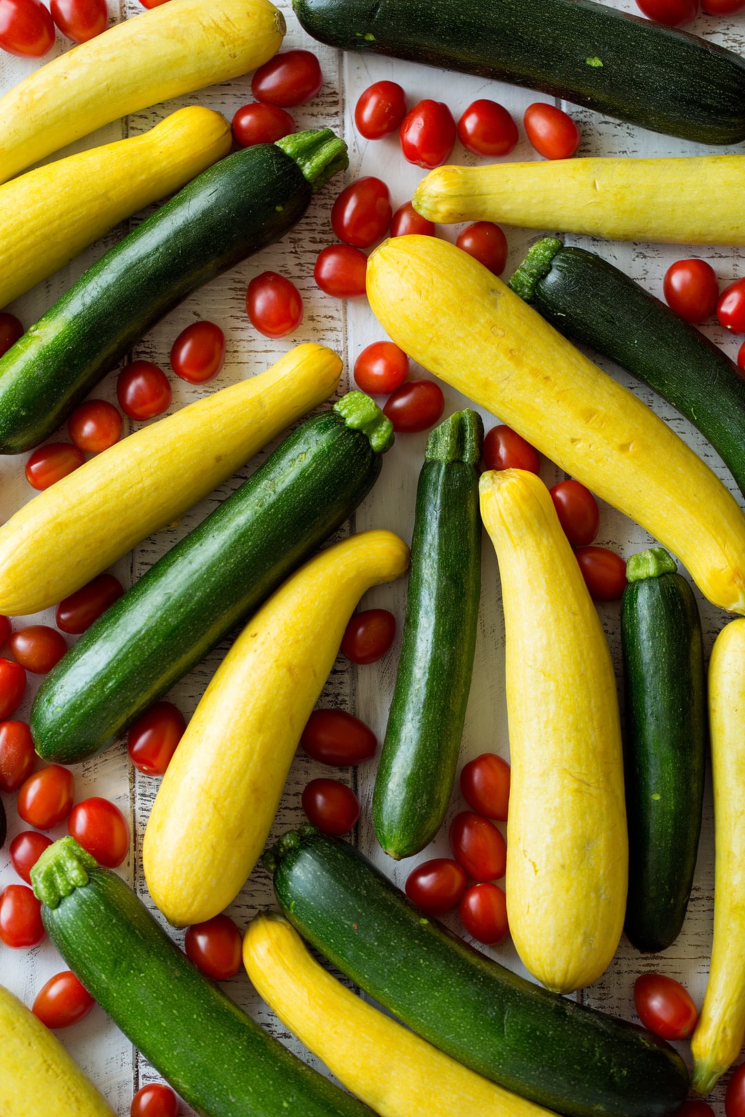 Garlic Parmesan Zucchini Squash and Tomatoes Image of fresh eight fresh zucchini, eight fresh squash and lots of fresh cherry tomatoes laying on a white wooden surface.
