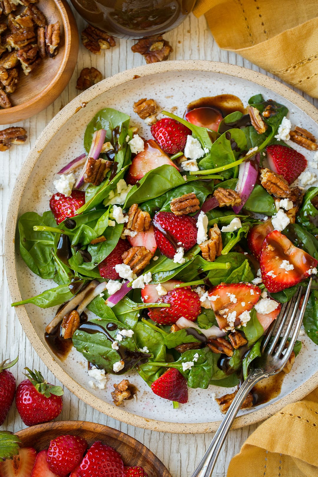 Strawberry Spinach Salad. An easy and delicious spinach salad made with strawberries, feta, candied pecans and a balsamic vinaigrette. | Strawberry Salad | Summer Salads | Easy Salads | #cookingclassy #spinach #strawberry #salad An overhead shot of a Strawberry Spinach Salad on a plate with chopped pecans