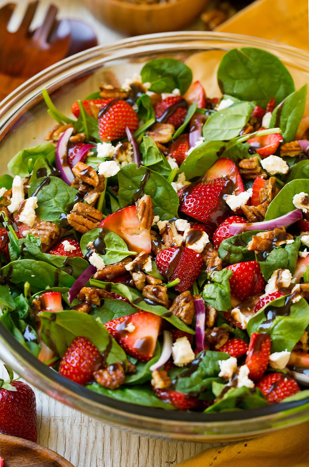 A close up of a Strawberry Spinach Salad in a glass bowl topped with a balsamic vinaigrette