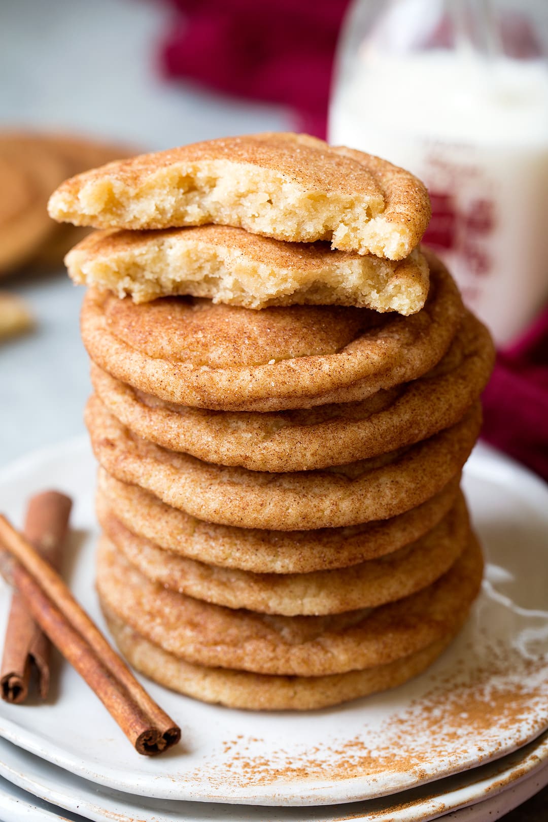 Snickerdoodle Cookies Stack of snickerdoodle cookies on a plate with one cooke on top broken in half to show texture of interior.