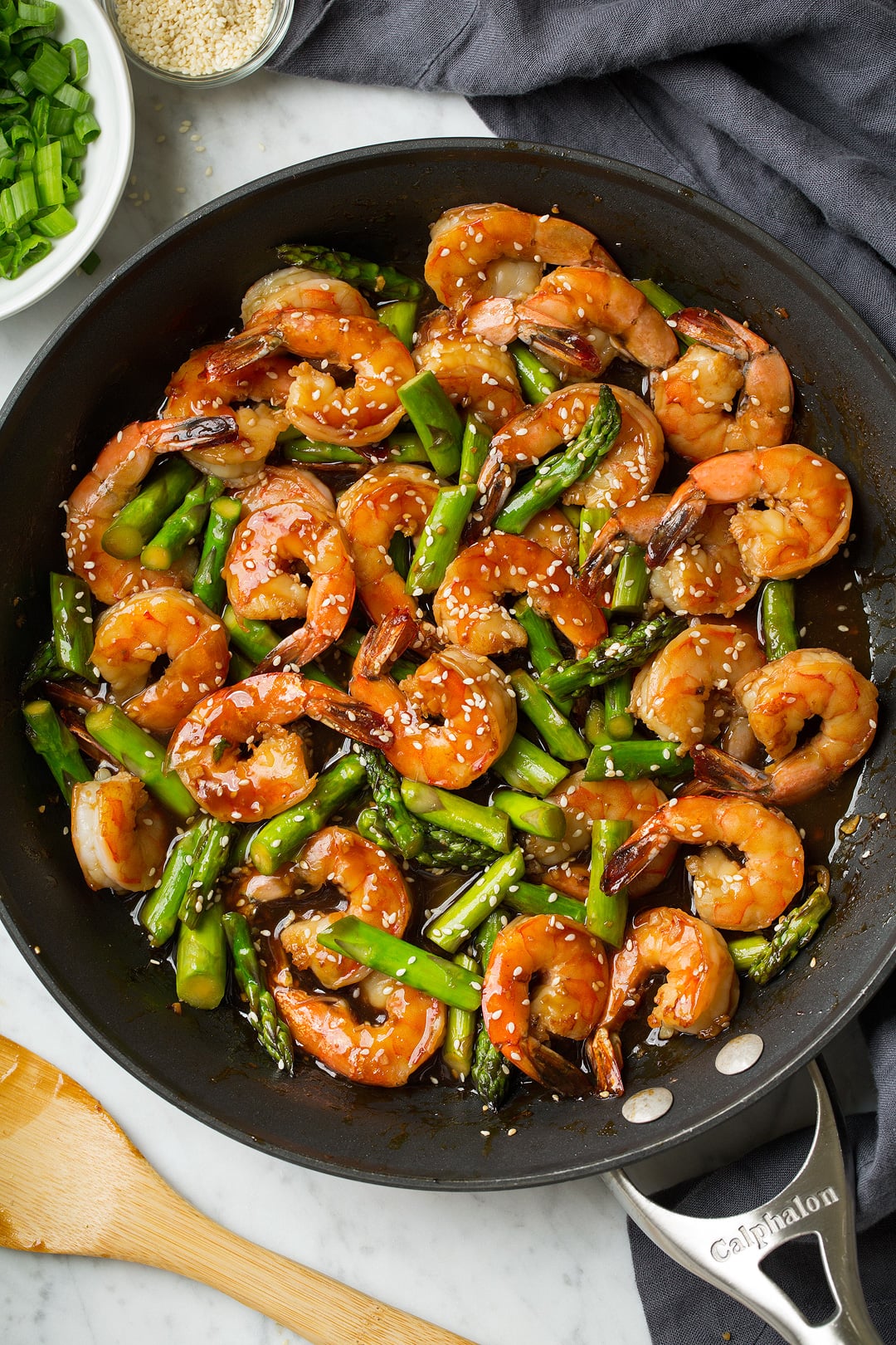 teriyaki shrimp and asparagus in a metal skillet with wooden spoon
