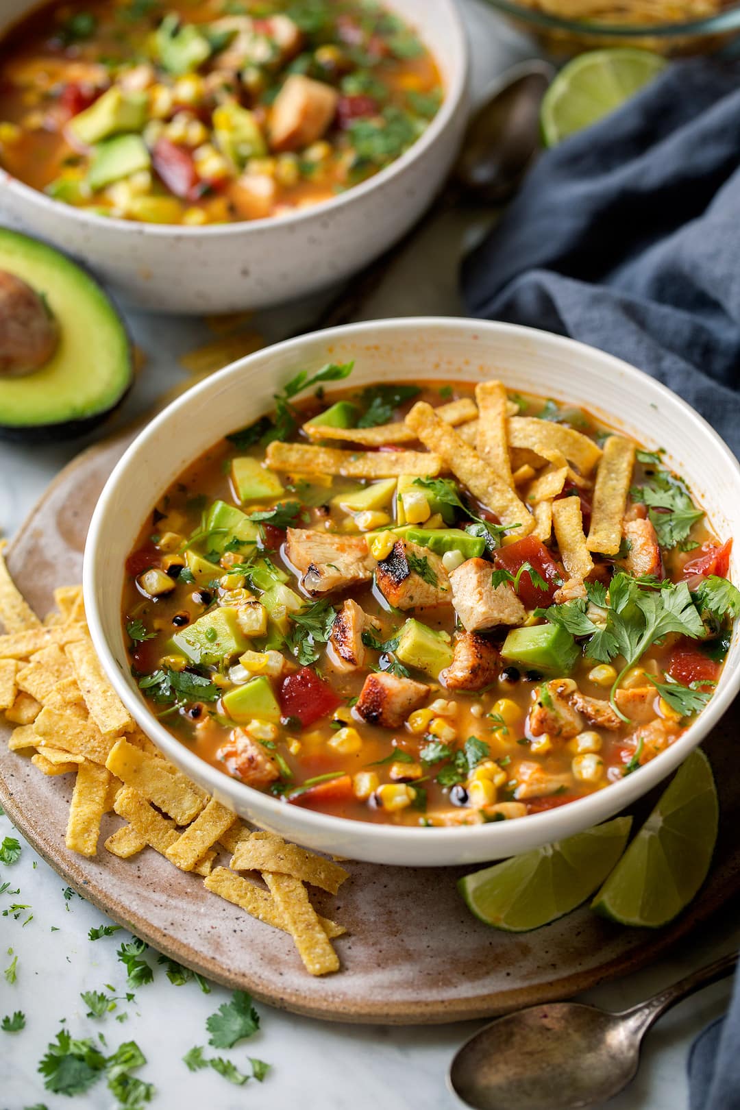 Traditional tortilla soup gets an upgrade with grilled chicken, grilled corn and plenty of diced avocados! Such a delicious summer soup! | Chicken Soup | Tortilla Soup | #cookingclassy #soup #chicken #comfortfood Grilled Chicken Tortilla Soup in a white bowl with tortilla chips at the side