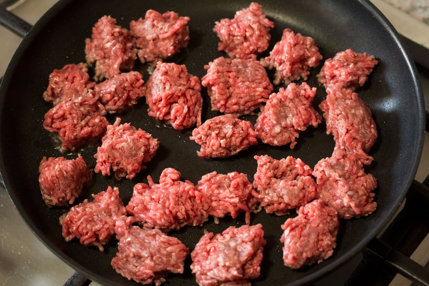 Korean Beef Bowls Raw ground beef added to a dark skillet in chunks.