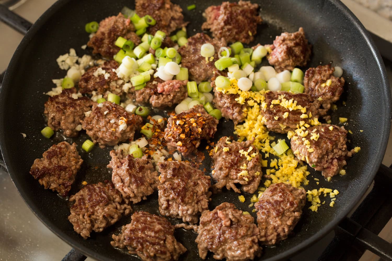Korean Beef Bowls Ground beef shown browned on one side with green onions, garlic and ginger added.
