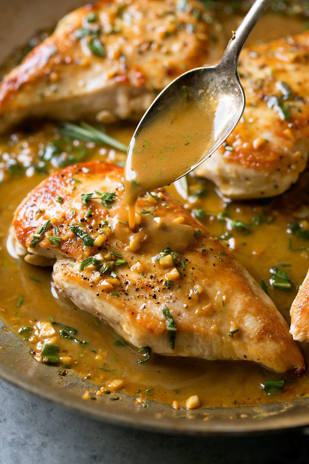 Super quick and easy seared skillet chicken topped with a delicious garlic and herb pan sauce that's sure to please! A perfect chicken recipe for busy weeknights. | Chicken Dinner | Chicken Recipes | Weeknight Meals | #cookingclassy #chicken #sauce #butter A butter sauce getting poured of Skillet Chicken with a spoon