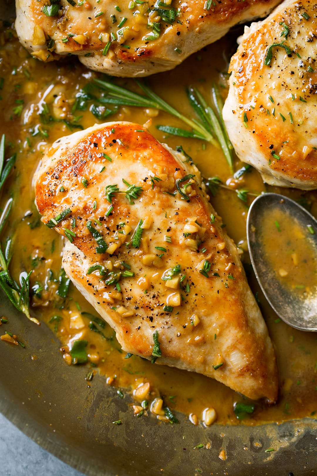 Super quick and easy seared skillet chicken topped with a delicious garlic and herb pan sauce that's sure to please! A perfect chicken recipe for busy weeknights. | Chicken Dinner | Chicken Recipes | Weeknight Meals | #cookingclassy #chicken #sauce #butter A close up of Skillet Chicken with Garlic Herb Butter Sauce in a pan with herbs and a spoon at the side