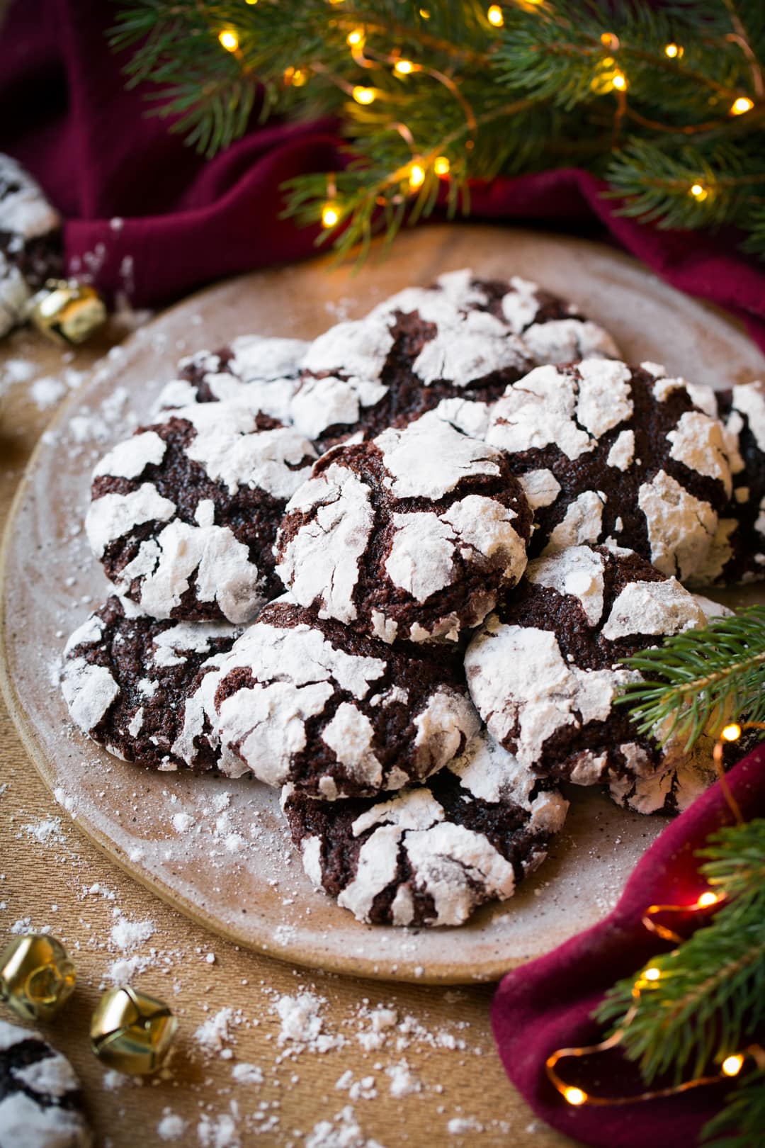 Chocolate Crinkle Cookies Chocolate Crinkle Cookies shown on a plate by a lit Christmas tree and red napkin.