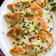 4 servings of chicken piccata on a white oval serving platter.