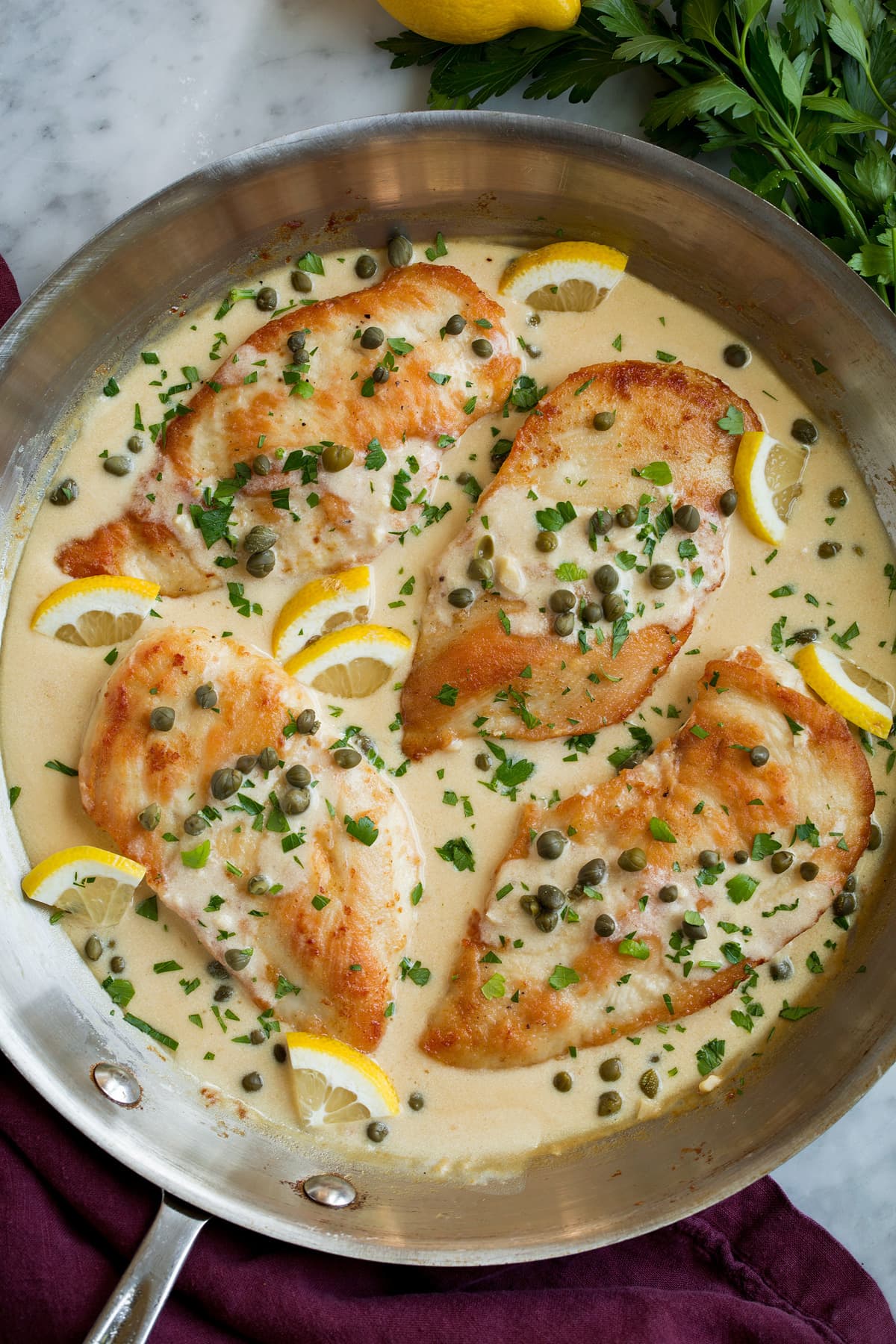 Chicken Piccata Four servings of chicken piccata in a creamy lemon piccata sauce, shown after cooking in a large aluminum skillet.