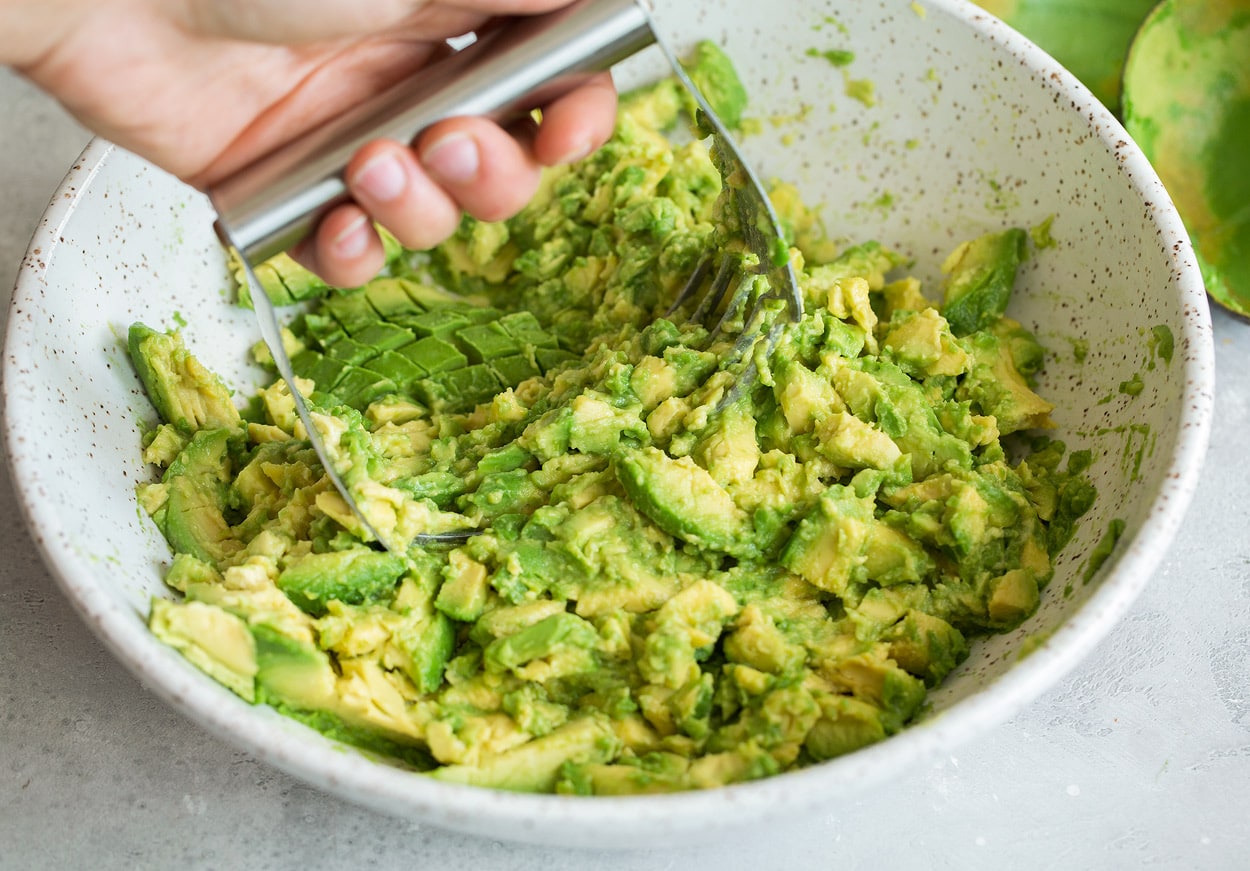 Homemade Guacamole Mashing avocados in a mixing bowl using pastry cutter to make homemade guacamole.
