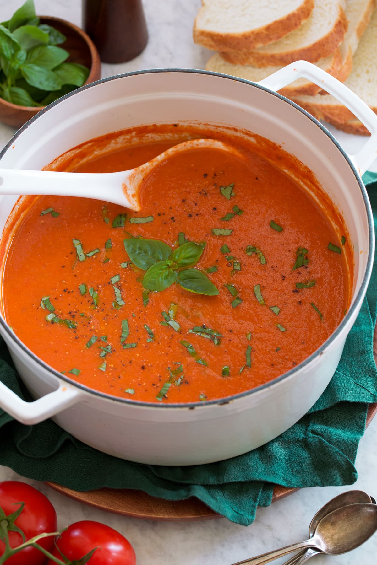 Roasted Tomato Basil Soup White pot filled with roasted tomato basil soup on a green cloth.