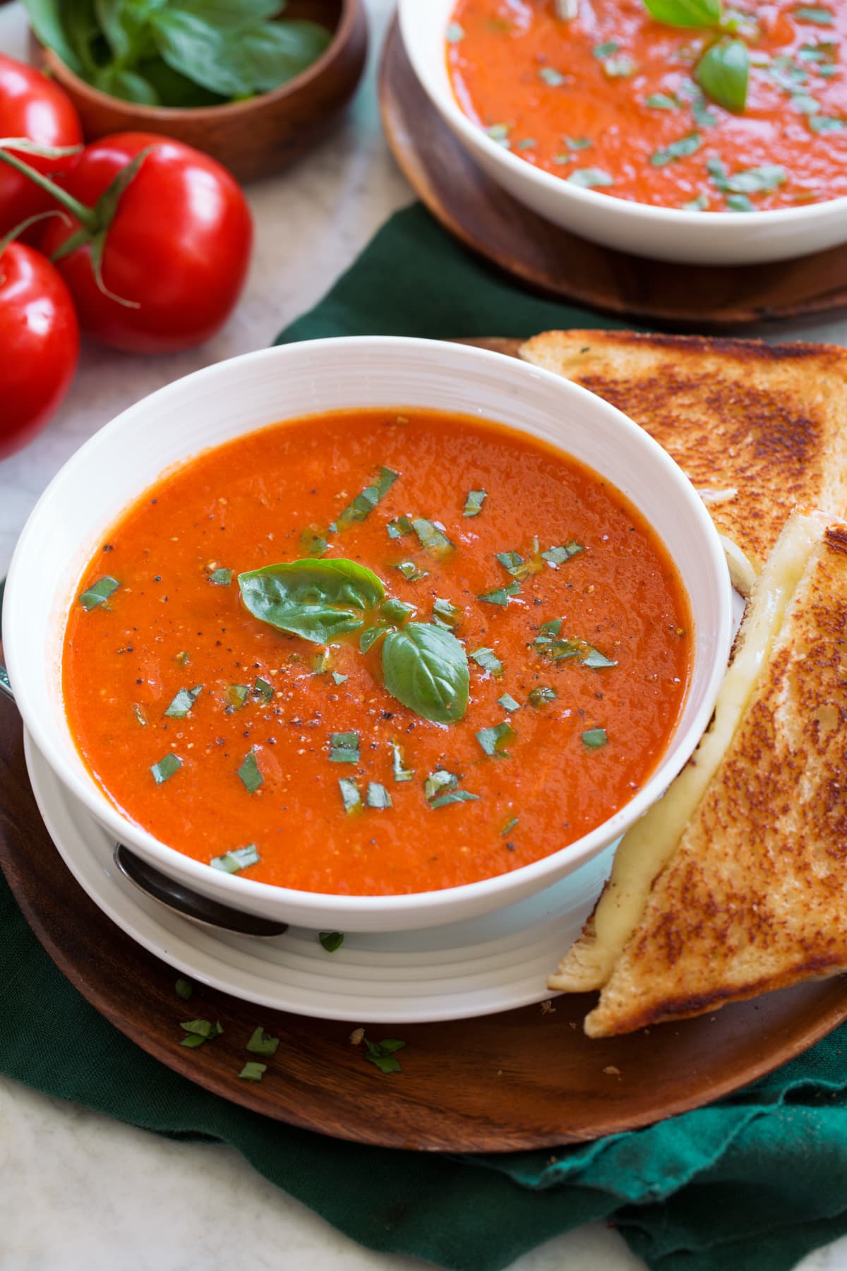 Roasted Tomato Basil Soup Serving of tomato basil soup shown close up in a white bowl with a grilled cheese to the side.