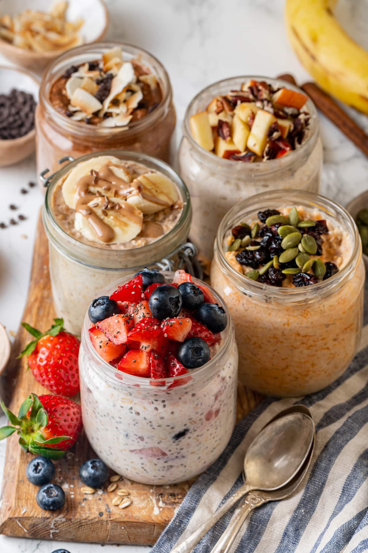 Learn how to make the best overnight oats that are rich, creamy, and perfect for breakfast on the go. Change it up with 5 amazing flavors! Overnight oats in mason jars, five different ways, on a wooden platter next to a spoon.