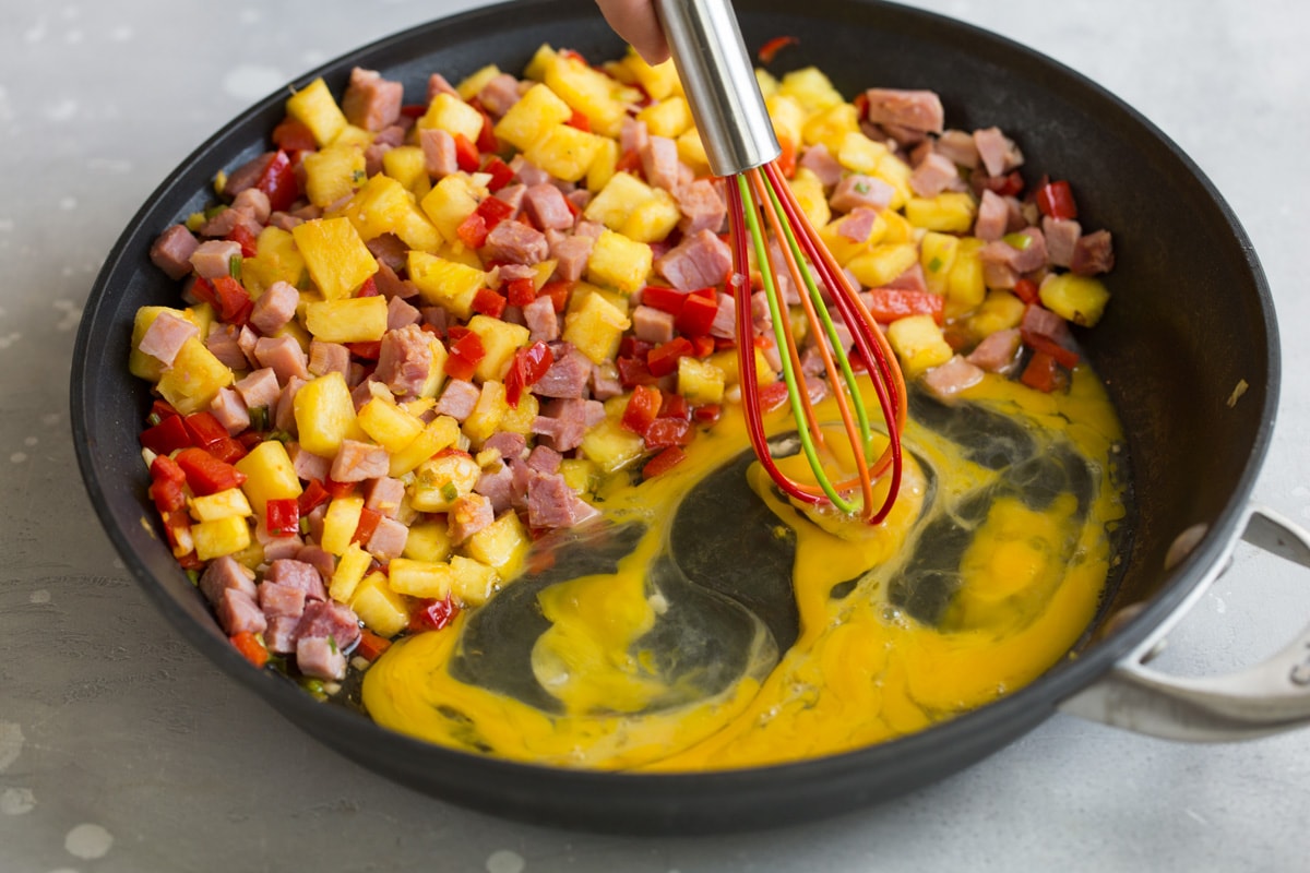 Hawaiian Fried Rice whisking eggs in a skillet next to pineapple ham and bell pepper mixture
