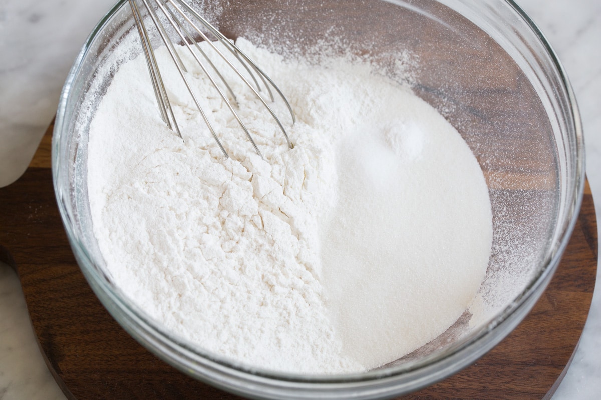 Peach Cobbler - the only peach cobbler recipe you'll ever need! I've never found better! Light and fluffy, buttery topping and perfectly sweet and juicy peach filling. #peach #cobbler #dessert #recipe Whisking flour and sugar in a baking dish to prepare fluffy biscuit topping for peach cobbler.