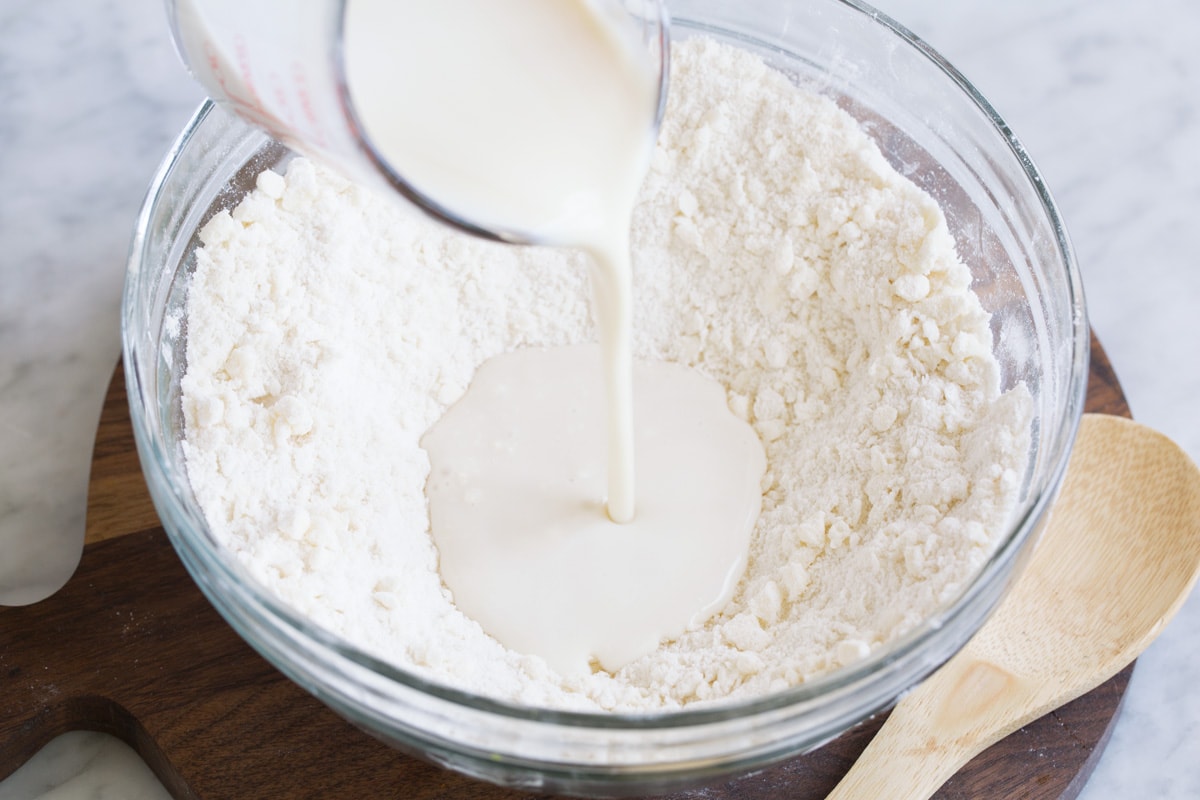 Peach Cobbler - the only peach cobbler recipe you'll ever need! I've never found better! Light and fluffy, buttery topping and perfectly sweet and juicy peach filling. #peach #cobbler #dessert #recipe Pouring buttermilk into well in flour mixture.