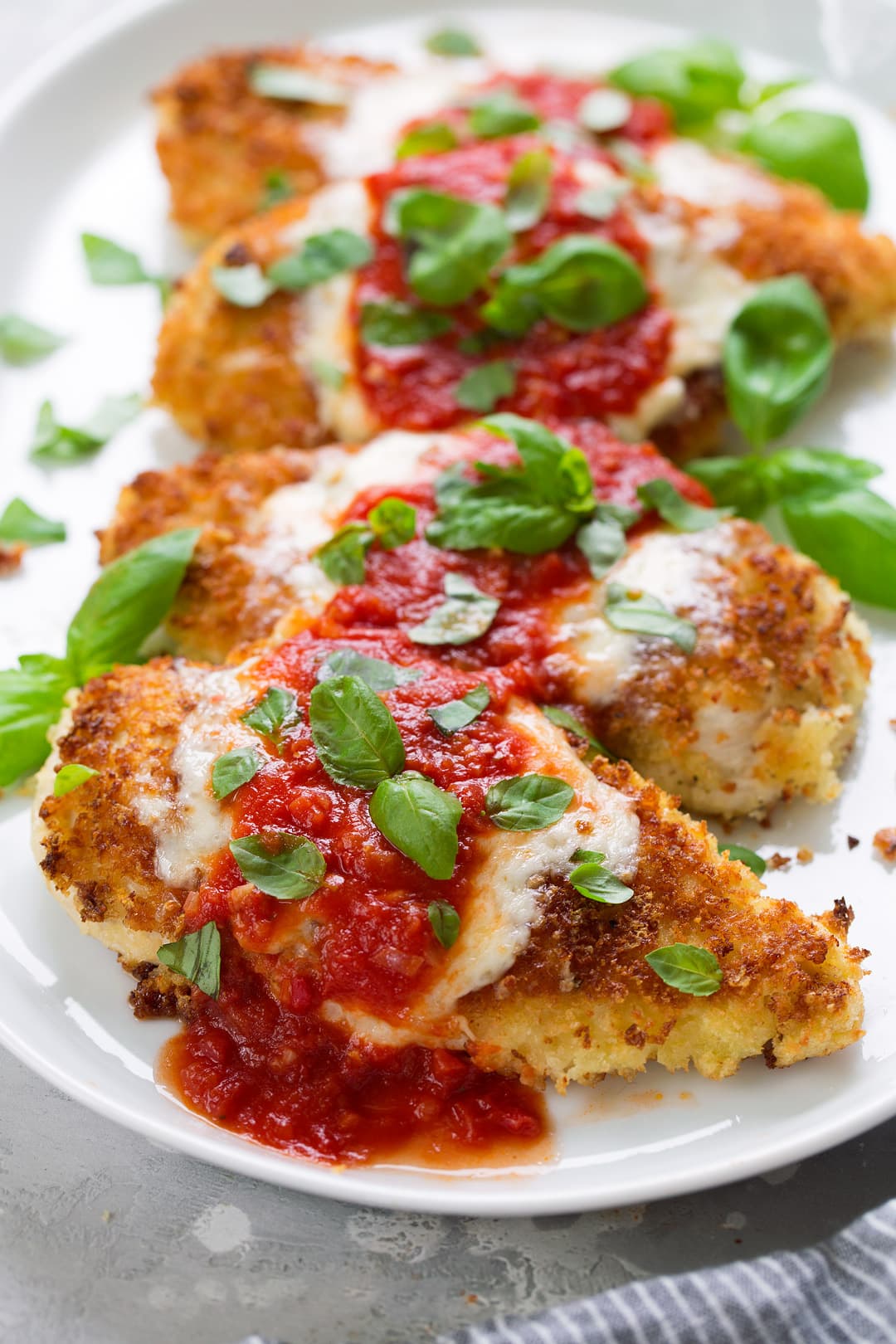 BEST Chicken Parmesan recipe! Row of four pieces of chicken parmesan on a white serving platter.