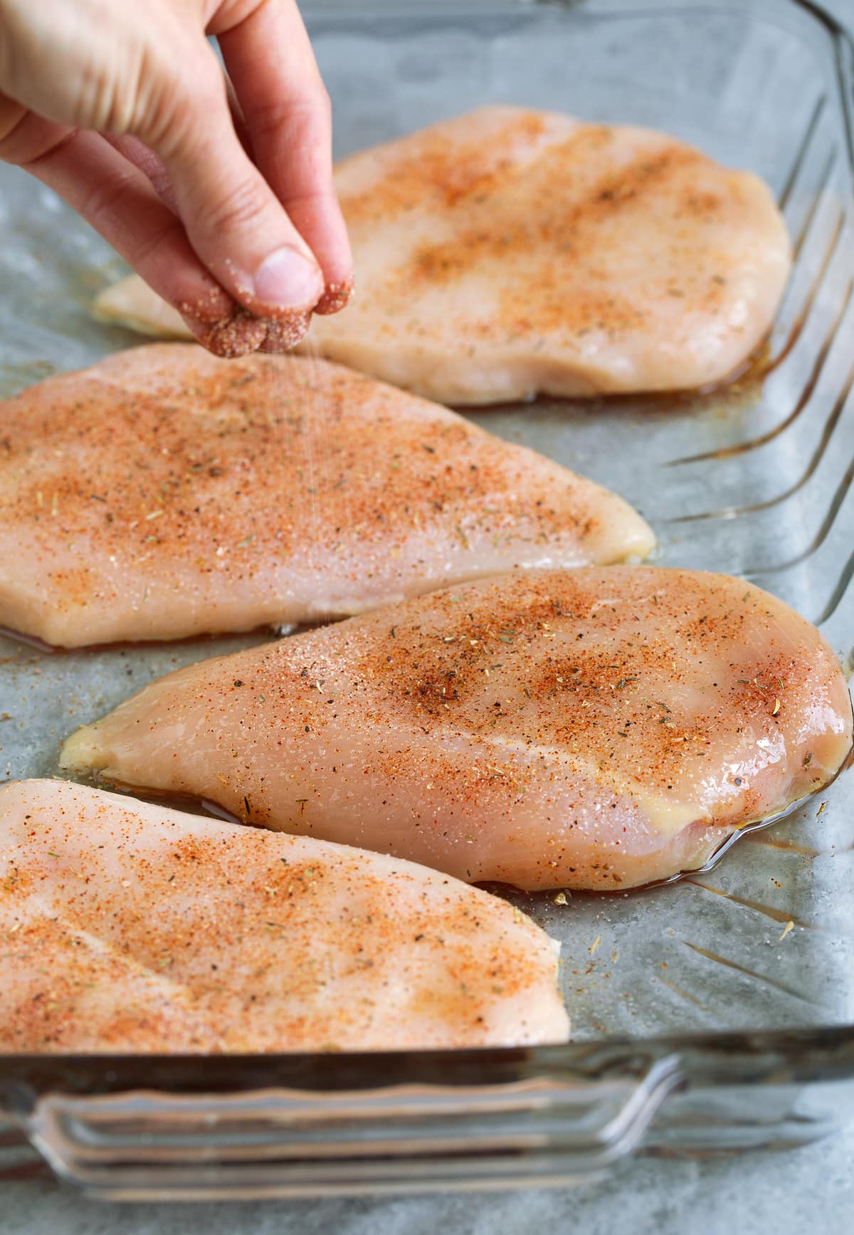 Baked Chicken Breasts Sprinkling seasoning mixture over raw chicken breasts in glass baking dish before baking.