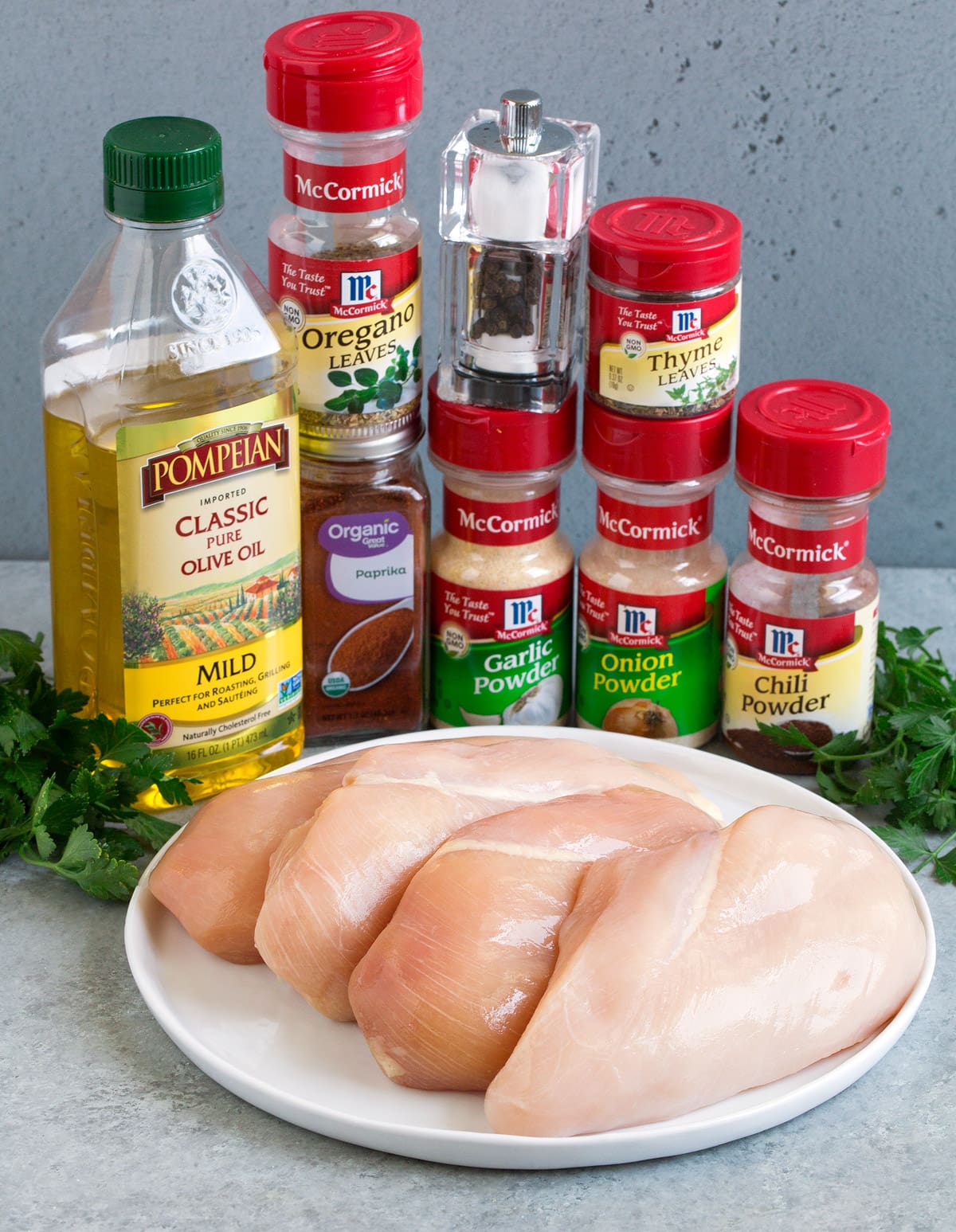 Baked Chicken Breasts Ingredients needed to make oven baked chicken breast shown here including small chicken breasts, chili powder, paprika, garlic powder, onion powder, thyme, oregano, salt pepper, olive oil and parsley.