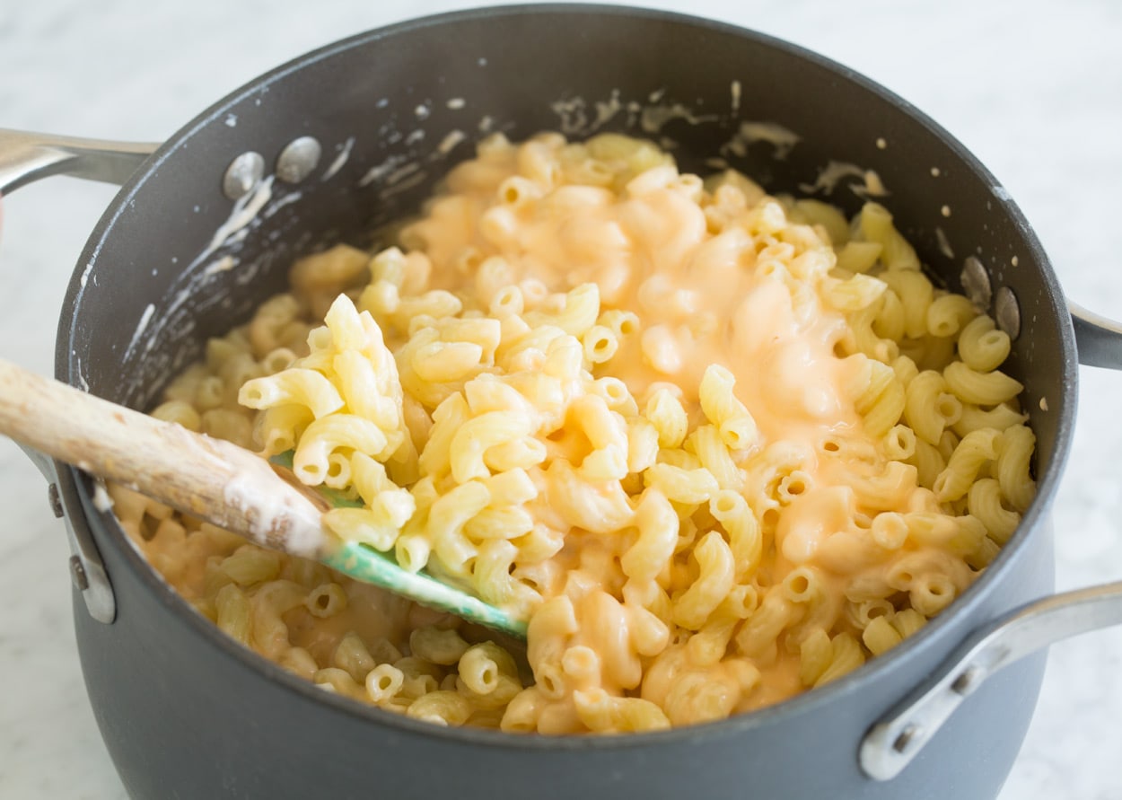 Mac and Cheese Tossing cooked pasta with mac and cheese sauce in pot.