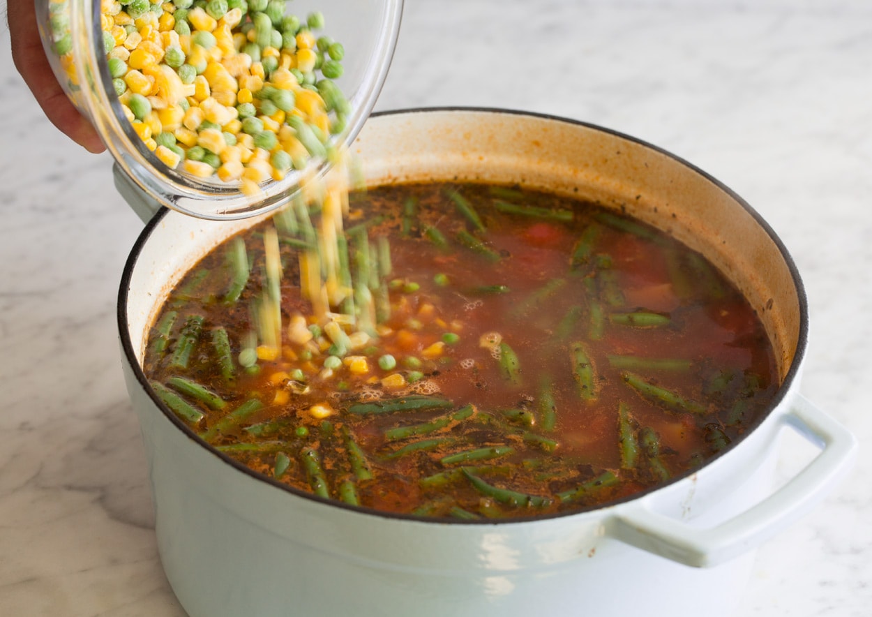 Vegetable Beef Soup adding frozen peas and corn to pot